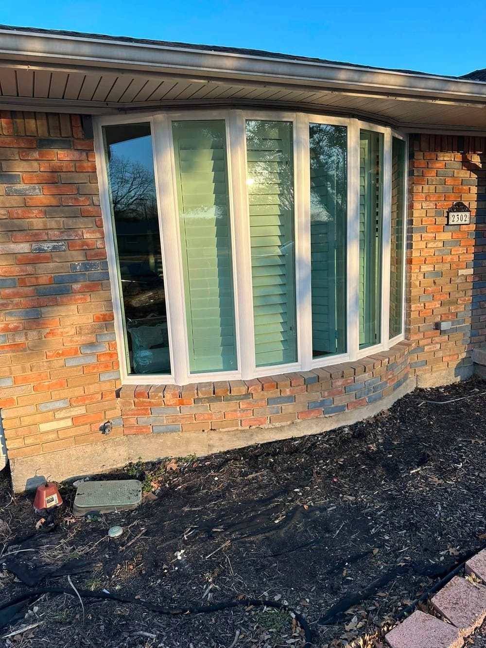 The same bow window rebuilt in white frames with clear glass, sitting on the original brick sill.