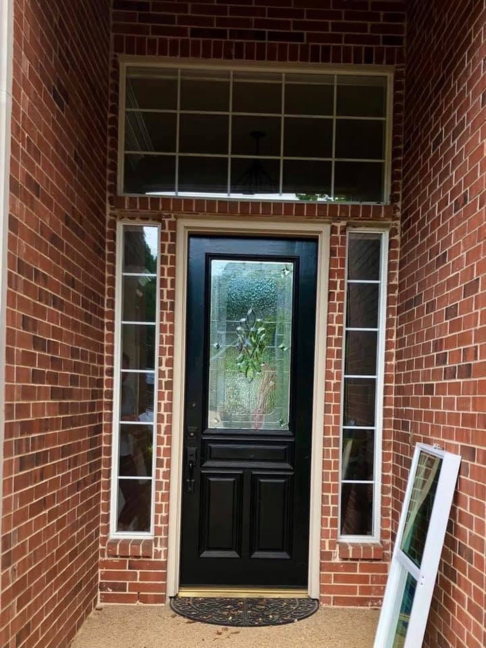 A black entry door with brass hardware, flanked by narrow sidelights under a gridded transom.