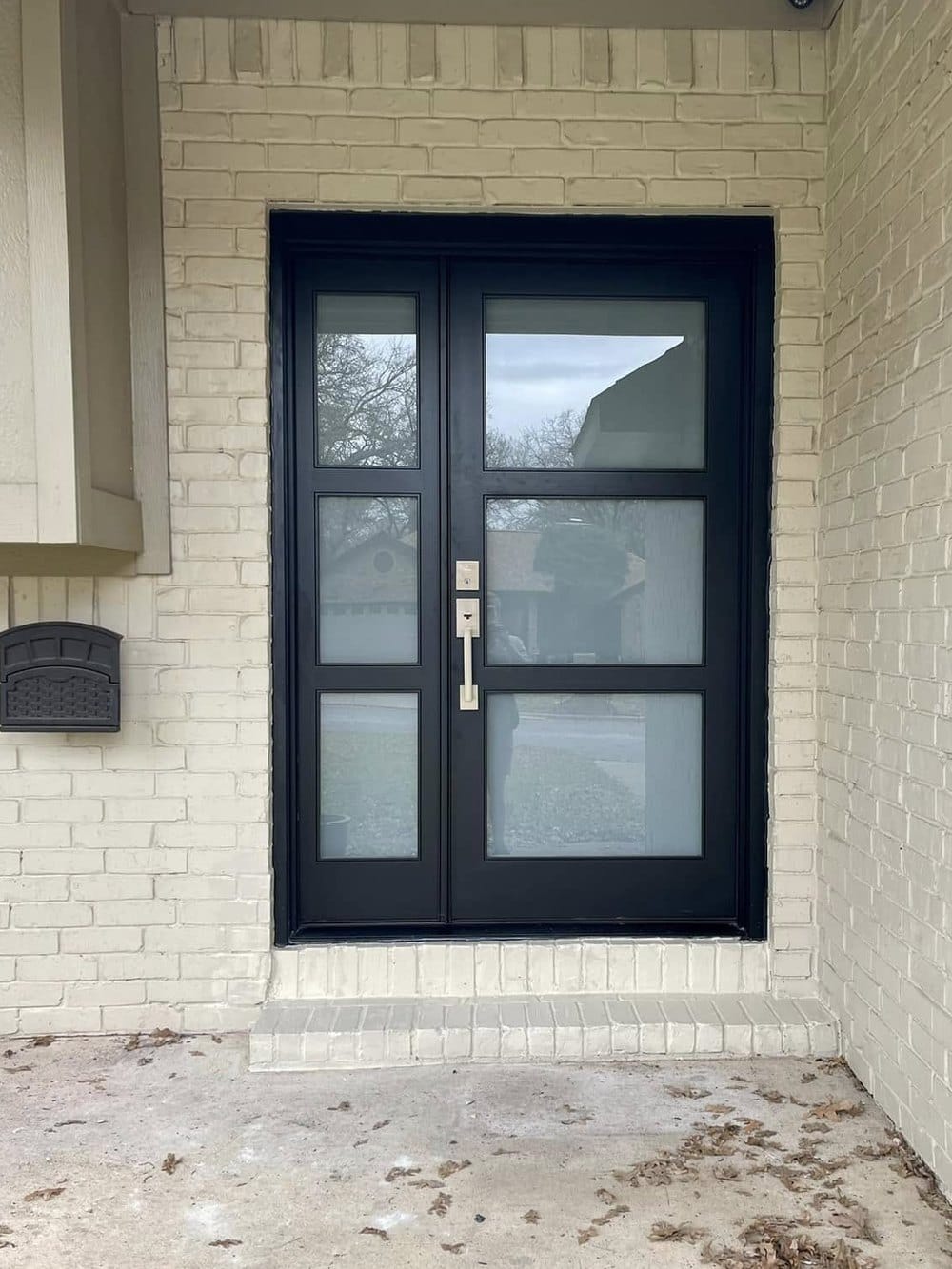 A modern black double entry door with frosted glass panels, set in a finished brick opening.