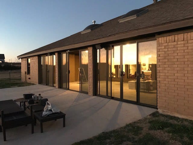 The same run of openings filled with black-framed sliding patio doors, lit from inside at dusk.