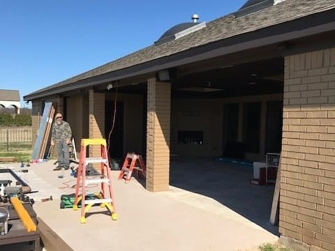 A covered patio mid-build, its openings still bare framing with a ladder and materials on the slab.