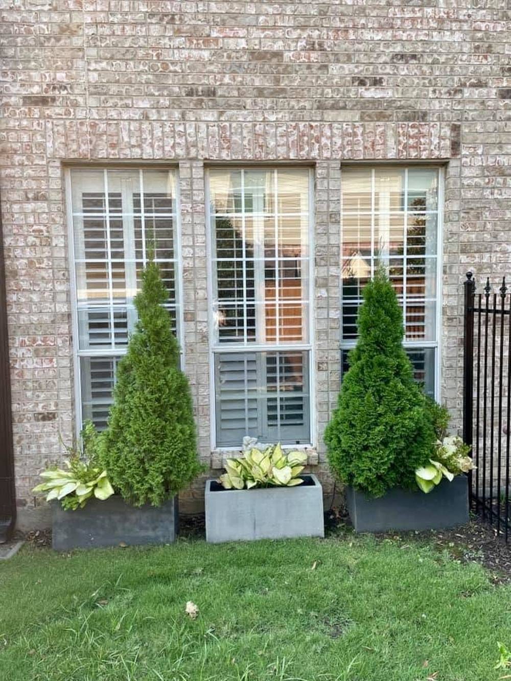 Three tall windows in a brick wall with white aluminum frames and grid inserts over every pane.