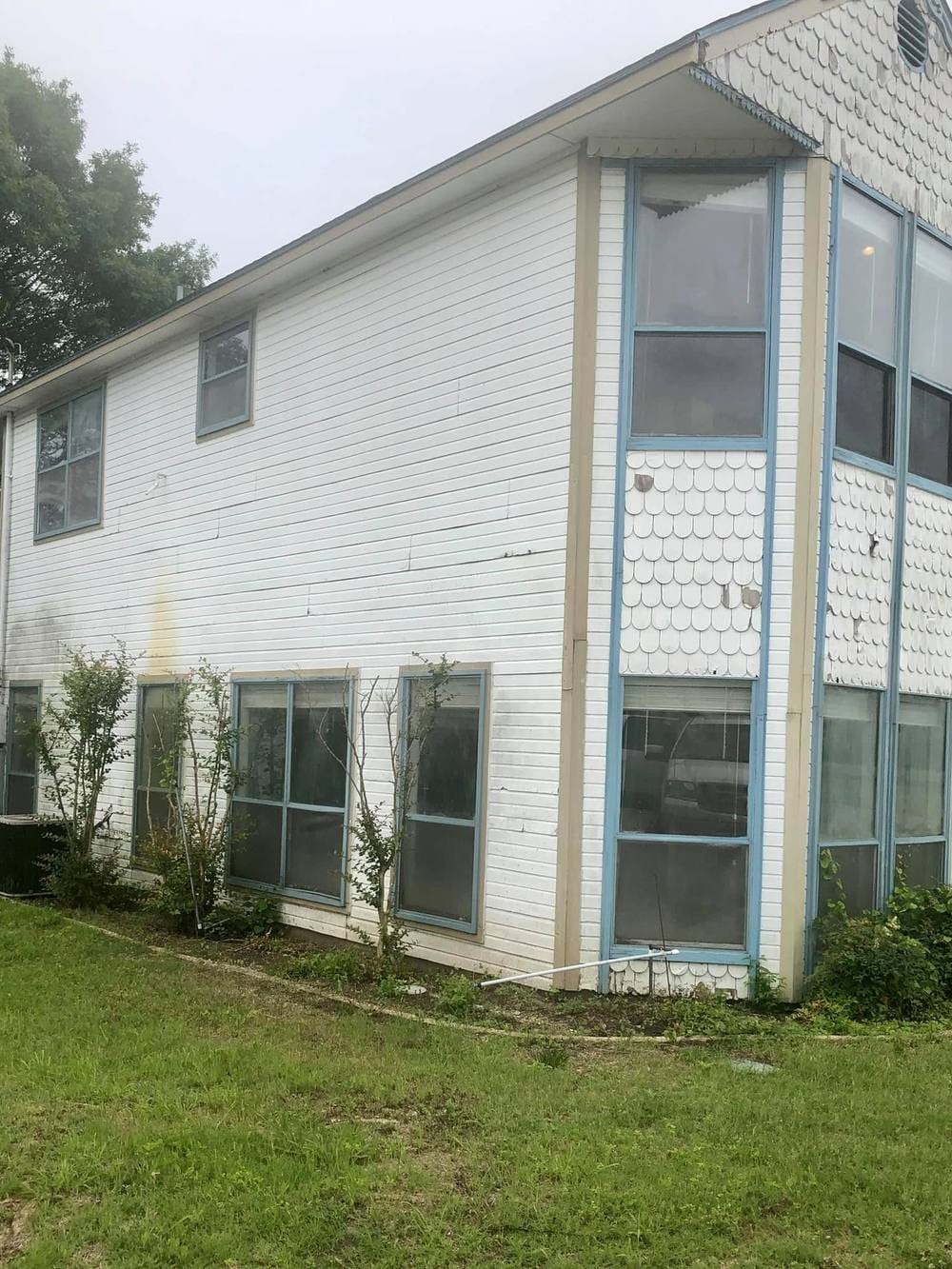 A weathered two-story home with peeling white siding and old blue-trimmed windows.
