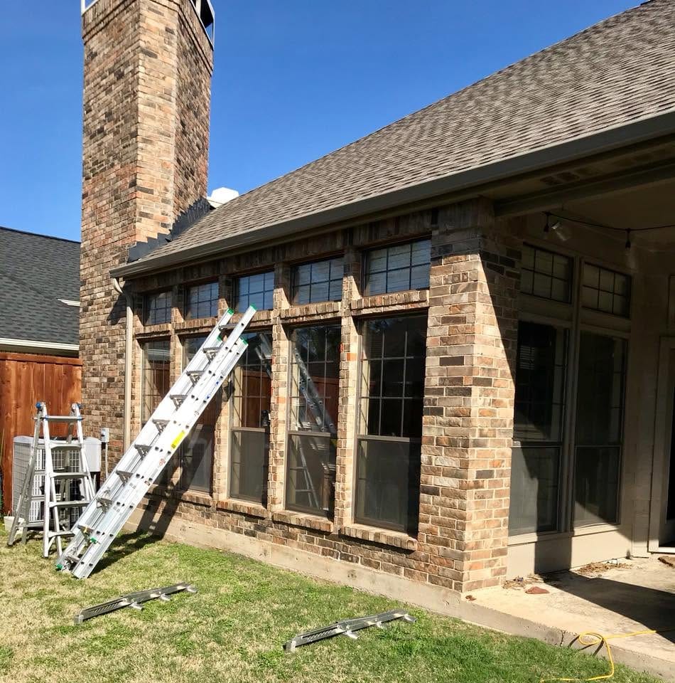 Ladders set up for a window replacement on a brick Texas home