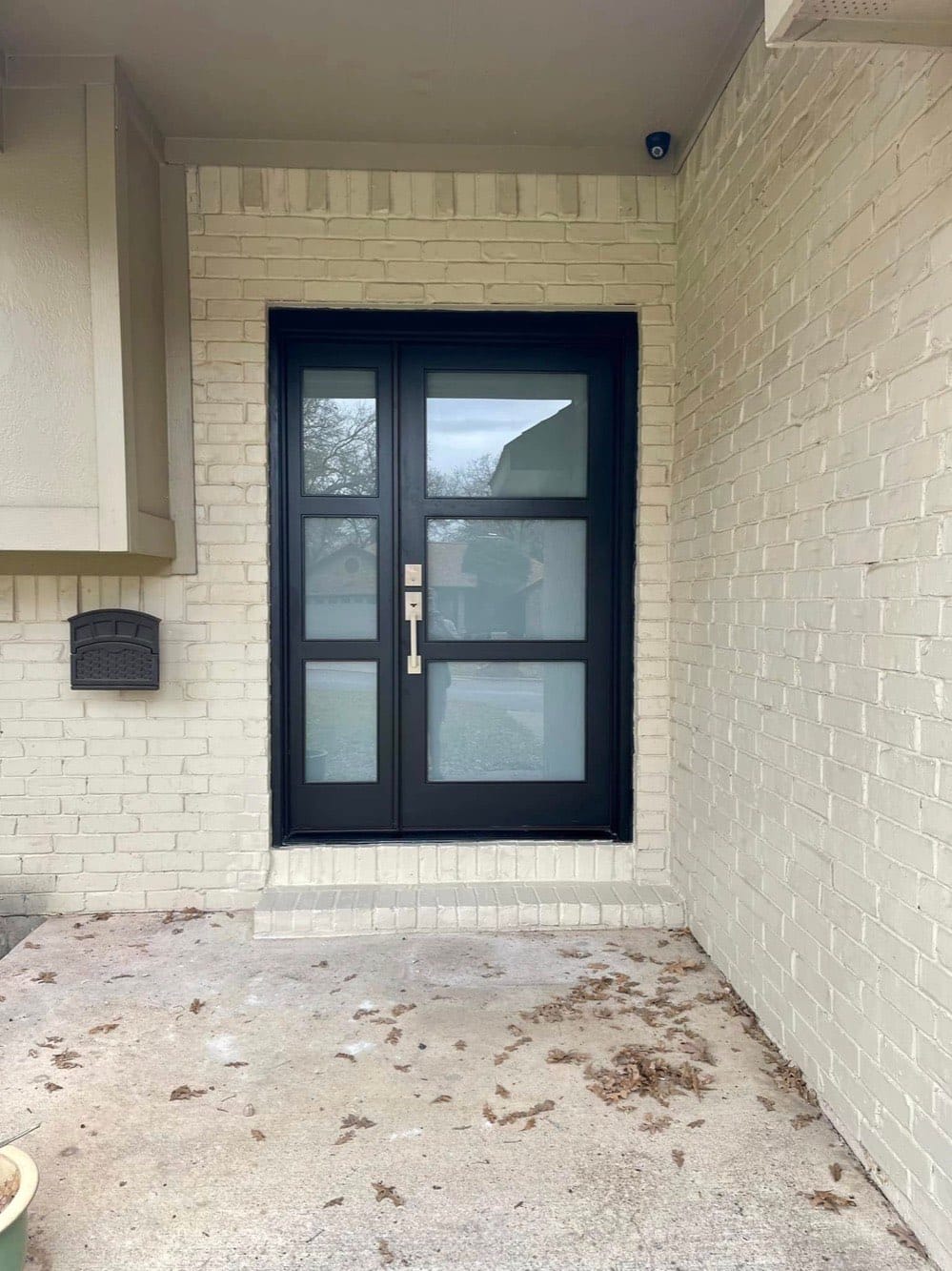A pair of black entry doors with frosted glass panels, newly fitted into a painted brick entryway.