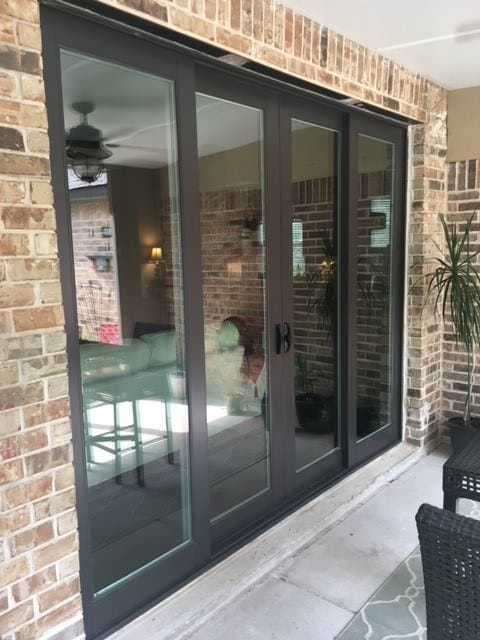 A four-panel black sliding French patio door in a brick wall, opening onto a covered patio.