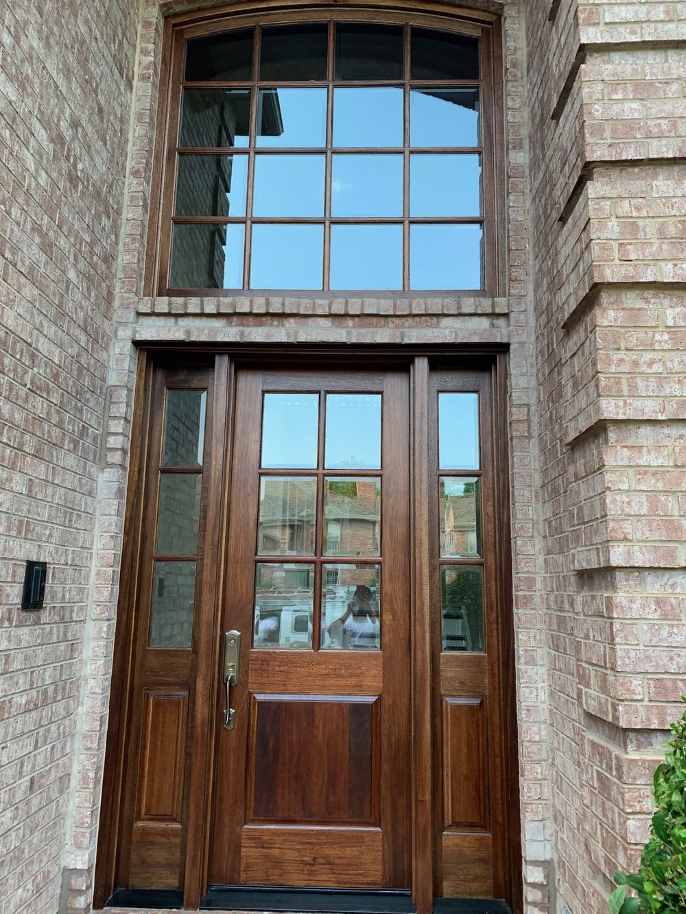 A stained wood entry door with divided-light glass, matching sidelights and an arched transom above, set in brick.