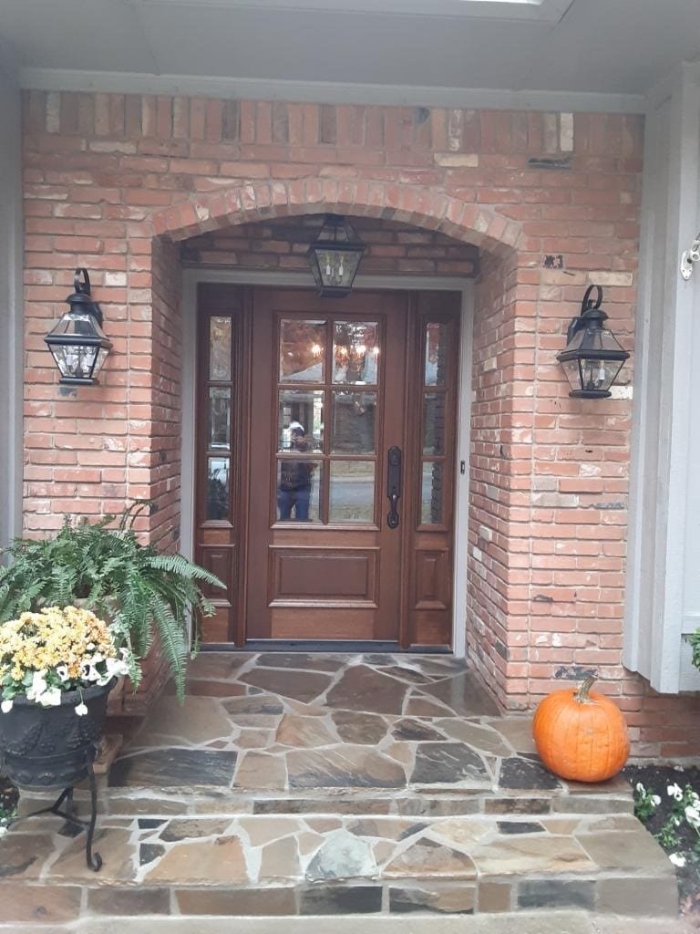 A stained wood entry door with glass sidelights under a brick arch, flanked by carriage lanterns.